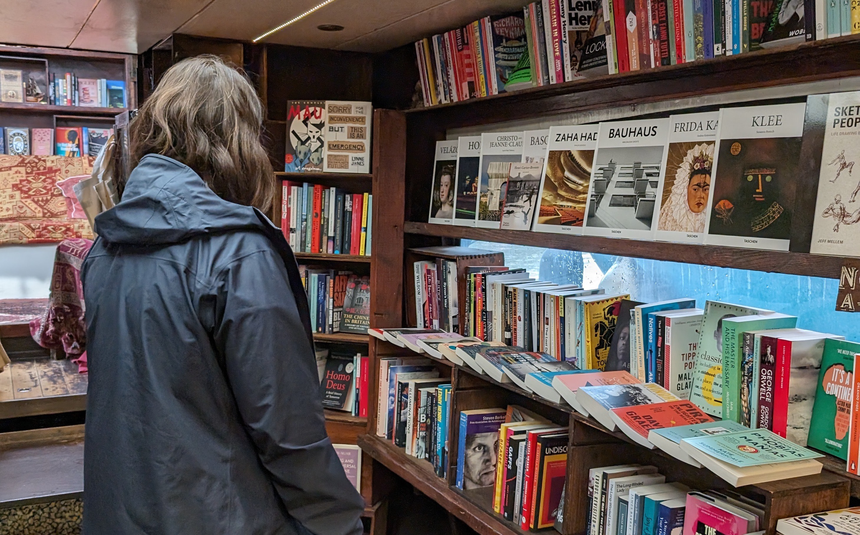 Photo of Bella standing in a bookstore on a canal boat. Bella is looking at a shelf of books.