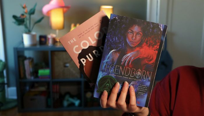 Photo in Bella's streaming room showing them holding up two books, Legendborn by Tracy Deonn and The Color Purple by Alice Walker.