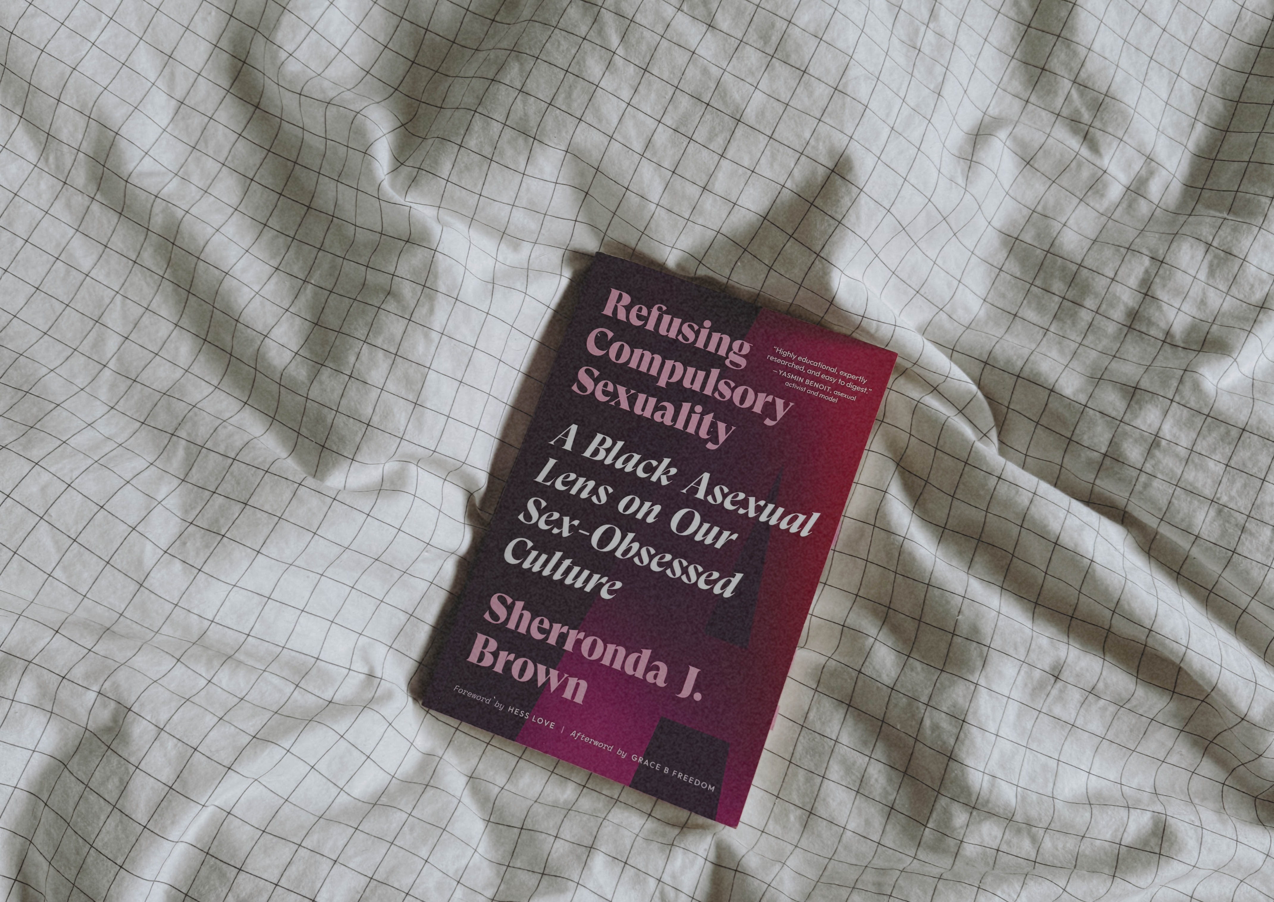 Photo of a purple book titled Refusing Compulsory Sexuality resting on a white checkered bedsheet.