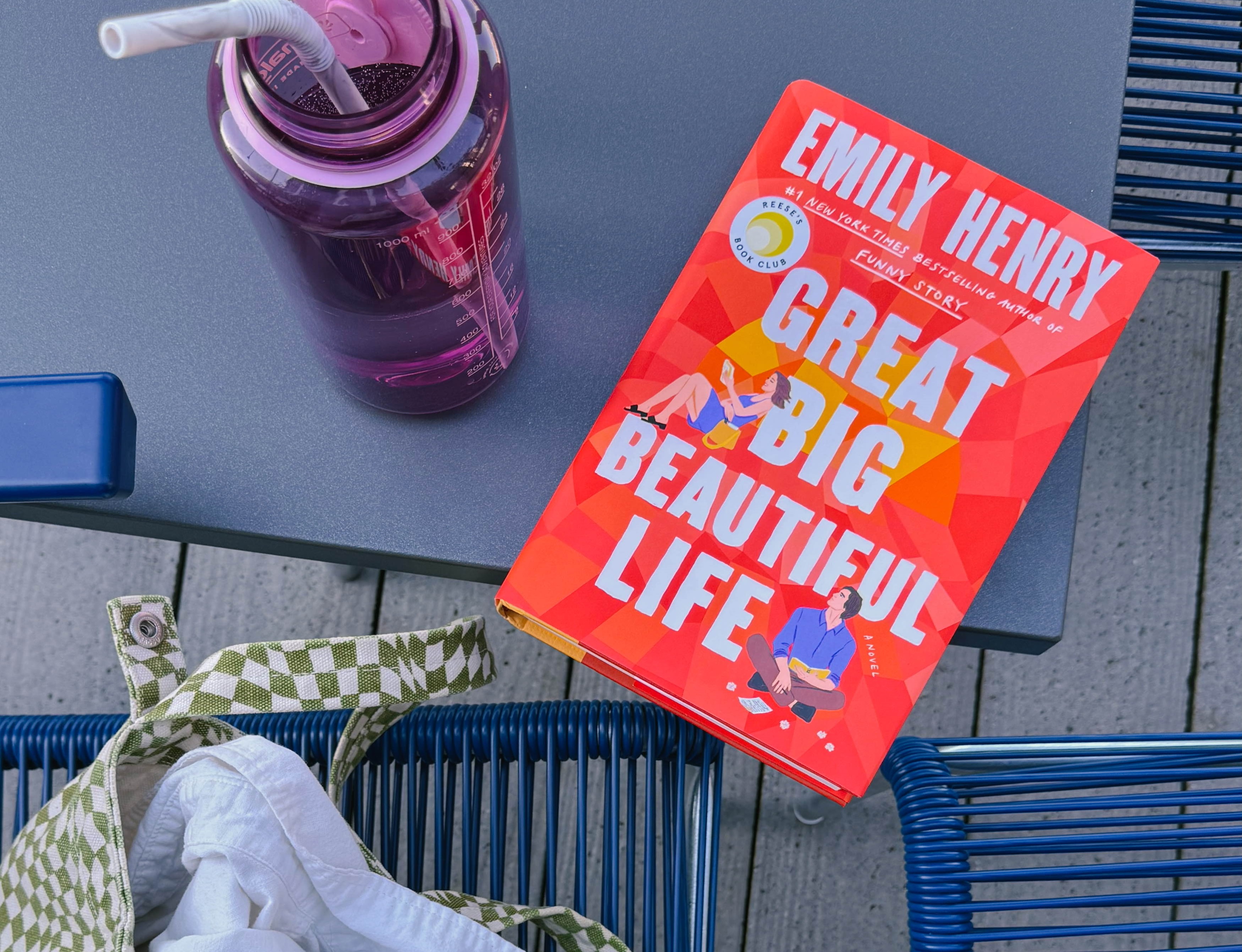Photo of the book Great Big Beautiful Life by Emily Henry resting on a table next to a water bottle and a green checkered bag.