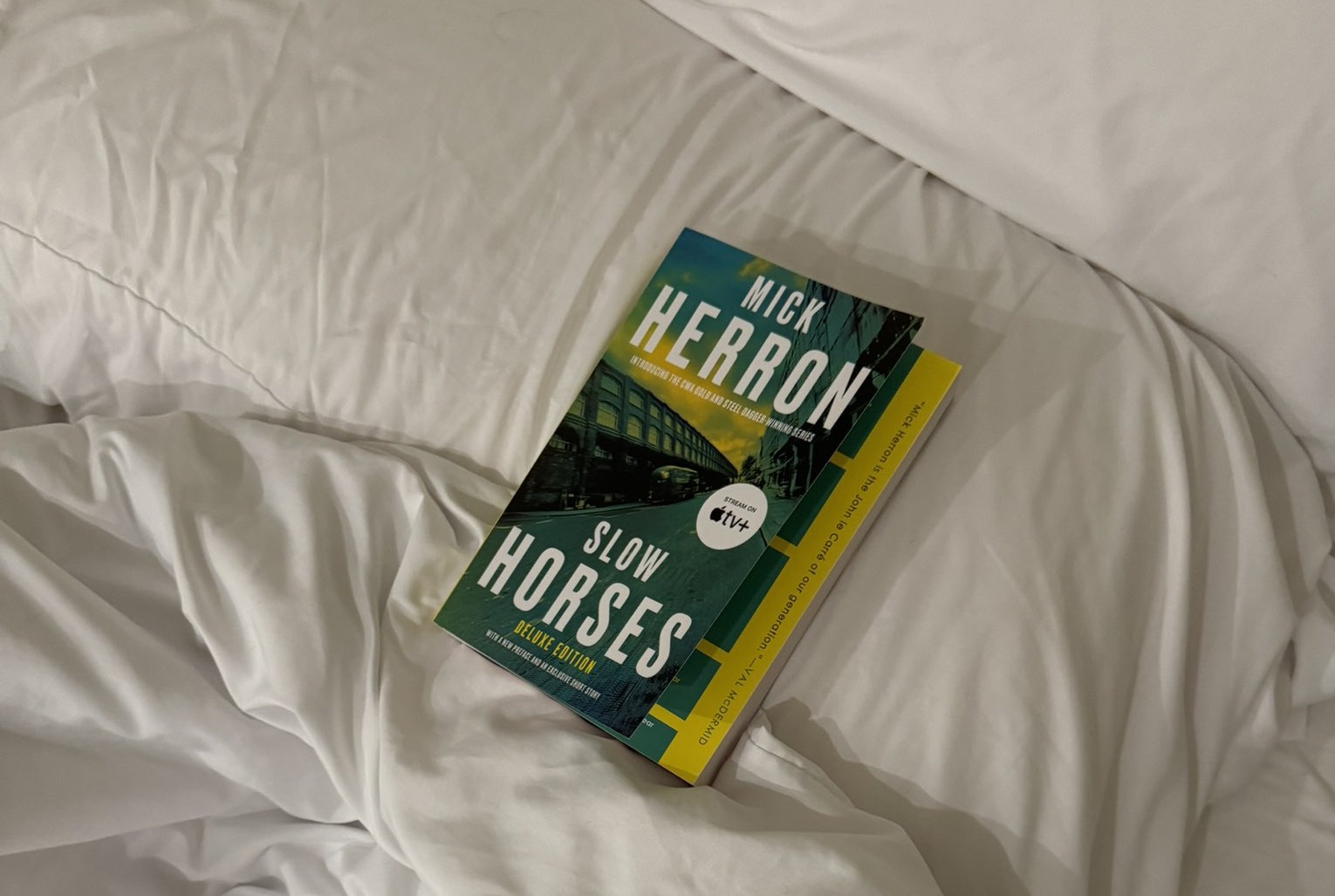 Photo of the book Slow Horses by Mick Herron resing on a bed with white sheets.